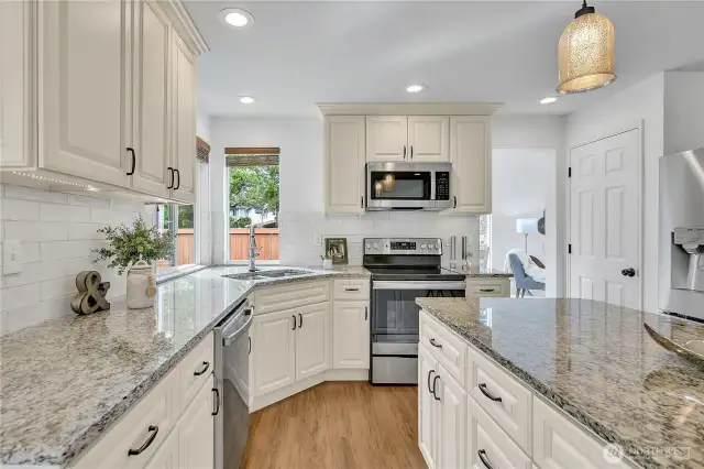 The stunning kitchen remodel showcases beautiful cabinetry with soft-close hinges, sleek slab granite countertops, and a full-height tile backsplash and under cabinet lighting that adds both style and