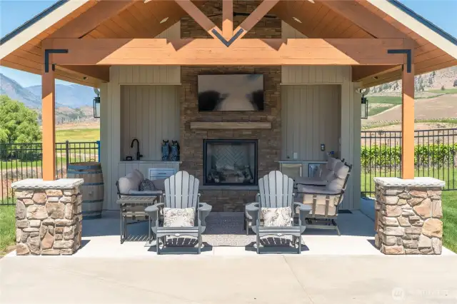 Covered pool lounge area equipped with a sink, beverage coolers, TV and propane fireplace