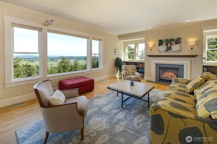 Warm and inviting living space centered around a fireplace, with expansive windows bringing in natural light and scenic views.