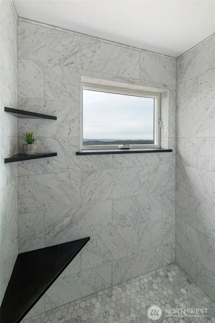 Custom tile walk-in shower with built-in shelving and window framing serene island views.