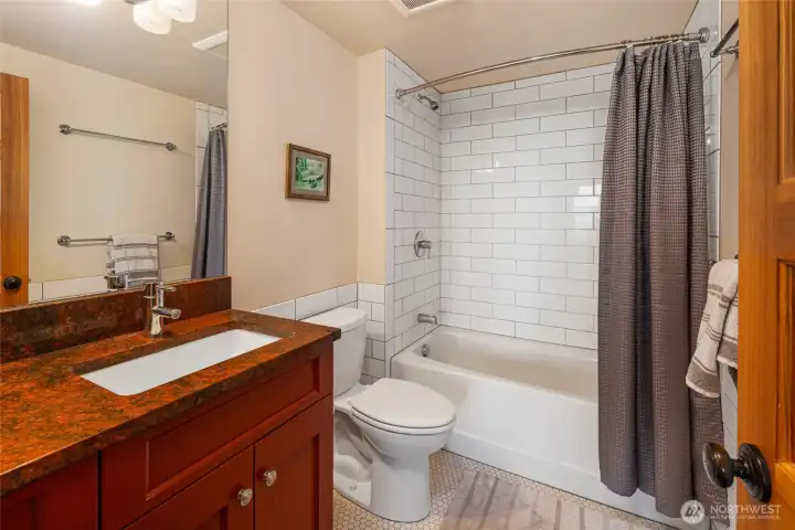 Well-appointed lower-level bathroom with tile surround tub/shower and stone countertop vanity.