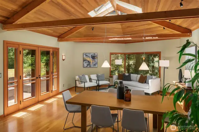 Vaulted ceilings, exposed wood beams, and hardwood floors frame the formal dining and living rooms, where French doors and ample natural light lead to an inviting entertaining deck.
