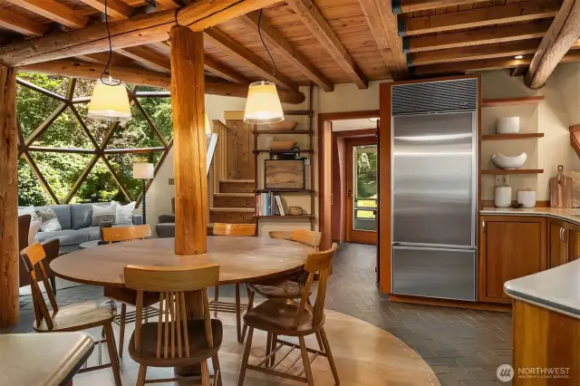At the heart of the home, the central dome reveals an open kitchen with a built-in dining table. Geometric dome windows blur the line between indoors and out, immersing you in the surrounding forest.