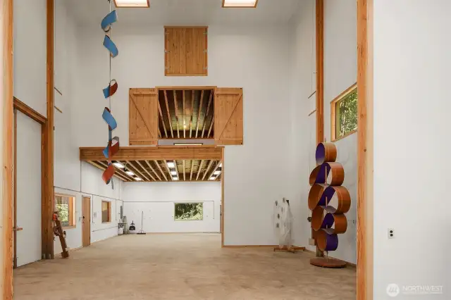 The shop features soaring three-story ceilings at its center, flanked by upper-level rooms on each side—accessible by stairs and equipped with barn doors, making it easy to lift heavy items via forklift.
