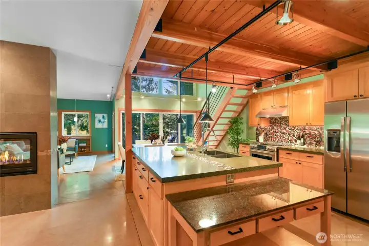 Kitchen view from entry foyer, living room to the left, dining room and deck access center, and stairs to loft above on right.  Primary bedroom door is on the right at the base of the stairs to the loft.