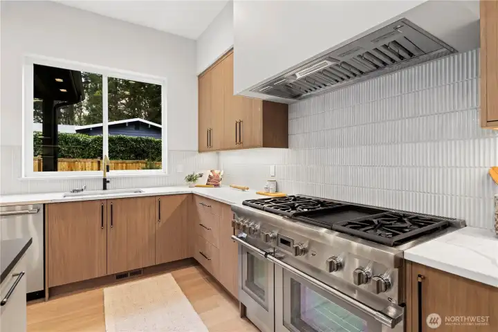 Thermador range with custom-framed hood. 6-burner, griddle, double ovens, and Wi-Fi enabled. Single-basin stainless steel sink with pull-out sprayer.