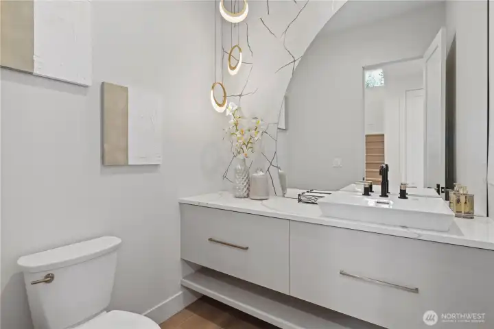 Tres chic! Main-level powder room with floating vanity, half-moon back-lit mirror, vessel sink and on-trend Alabaster and gold rimmed pedant lights.