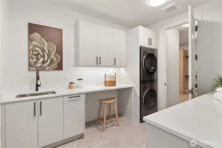 Well-appointed laundry room: base and upper cabinets, LG stacked washer and dryer, stainless utility sink with pull-out sprayer, pull-out  garbage, slab quartz folding counters, under cabinet lighting, and toe-kick motion sensor. Laundry connects directly to the primary walk-in closet.