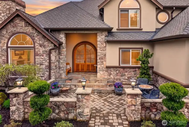 A handcrafted arched wood-and-glass double door, stone columns, and a paver courtyard create a warm, welcoming first impression that guests will remember. The slate steps and front door create an inviting feeling, and are ready to greet years of visitors.