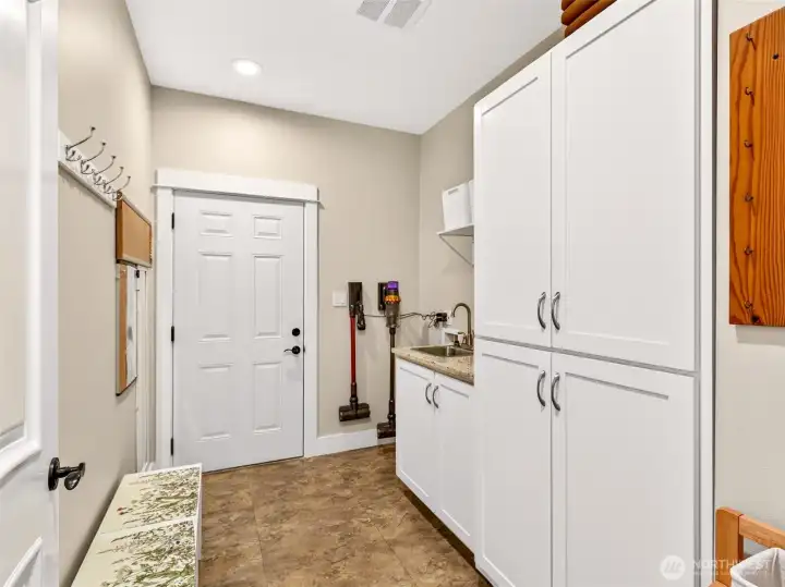 A spacious mudroom just off the garage features custom cabinetry, a utility sink, hooks for coats and keys, and a second laundry hookup for ultimate convenience. Drop-zone organization that keeps daily life running smoothly.