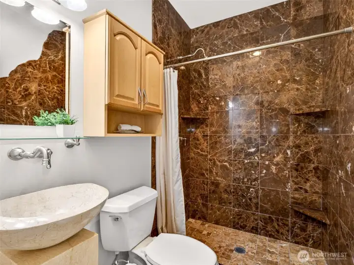 The main-level three-quarter bath features a stylish marble-tiled shower, vessel sink, and warm wood accents for guest-ready comfort. A thoughtful touch of luxury for visitors and everyday use alike.