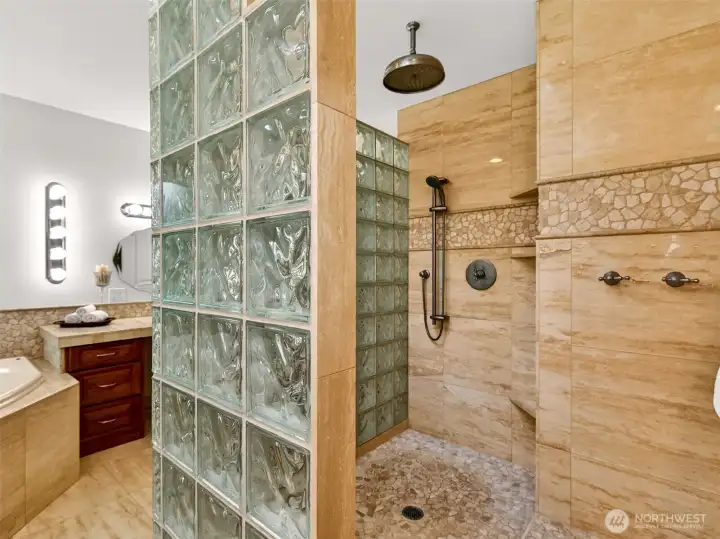 A walk-in travertine shower with rain head, handheld wand, and stunning glass-block partition creates a luxurious spa experience right at home. Heated travertine floors add warmth underfoot year-round.