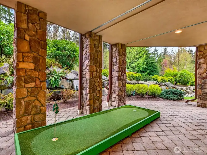 A covered lower patio features an included putting green tucked between artisan stone columns, perfect for honing your short game year-round. Pacific Northwest weather is no match for this protected outdoor escape.
