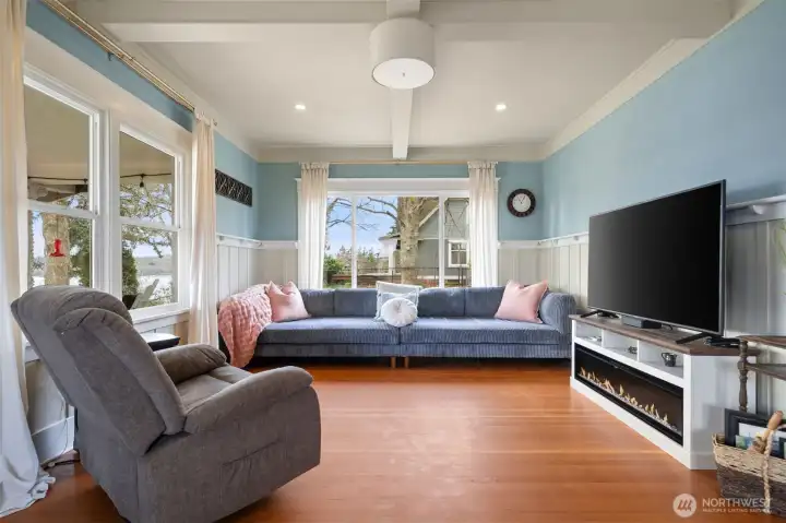 Living room with fir flooring high ceilings, faux beams, wainscoting and territorial view through the windows through the covered porch.