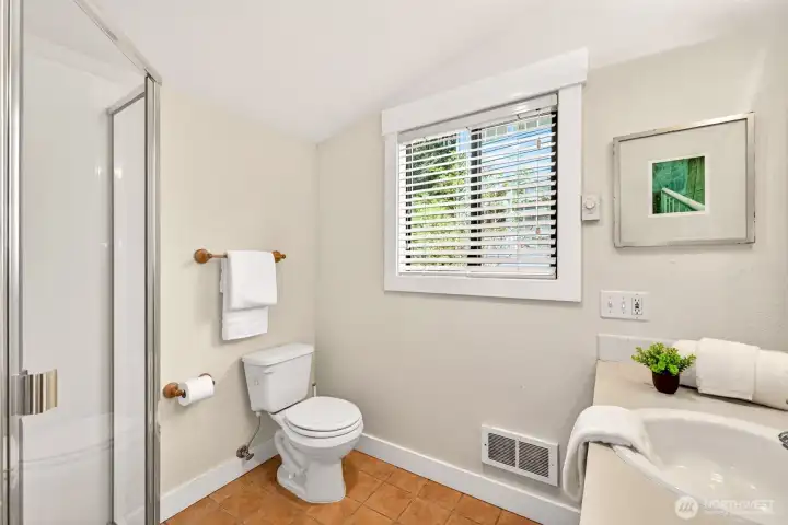 A convenient three-quarter bath on the main level features a glass-enclosed shower and bright window, ideal for guests or post-garden cleanup.