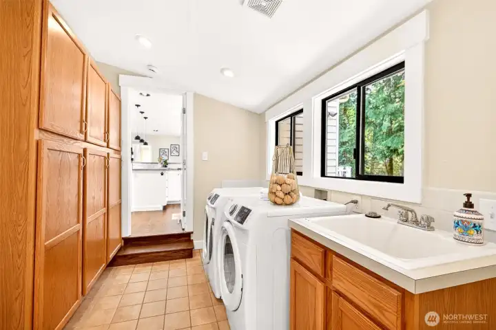 A spacious dedicated laundry room with side-by-side washer and dryer, deep utility sink, abundant cabinetry, and natural light keeps everyday chores organized and out of sight.