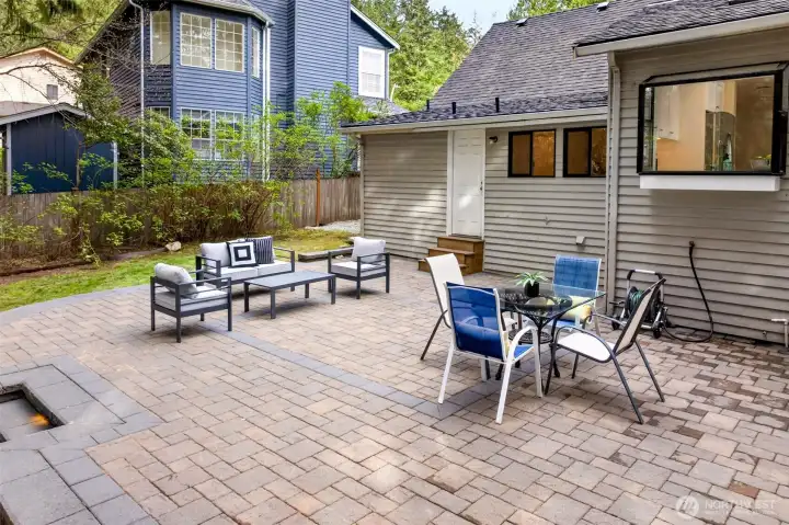 The two-tier outdoor living arrangement combines a dining zone with a comfortable conversation area, all on the new stone paver patio designed for effortless backyard hosting.
