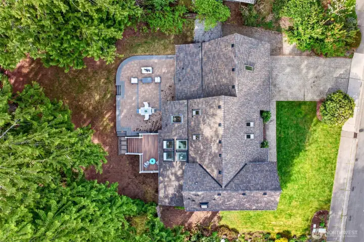 An overhead view captures the home's smart footprint, the substantial new paver patio with deck extension, and the wooded buffer wrapping the back of the lot.
