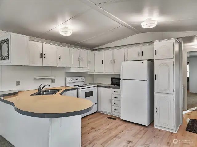 A bright and refreshed kitchen with newly painted cabinets featuring modern hardware. White appliances keep the space light and airy. The new flooring ties everything together beautifully.