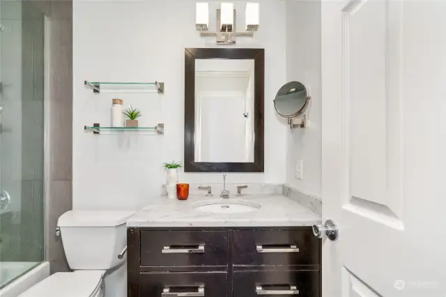 Updated bathroom with Carrara marble vanity, surround tile and custom enclosed tub/shower.