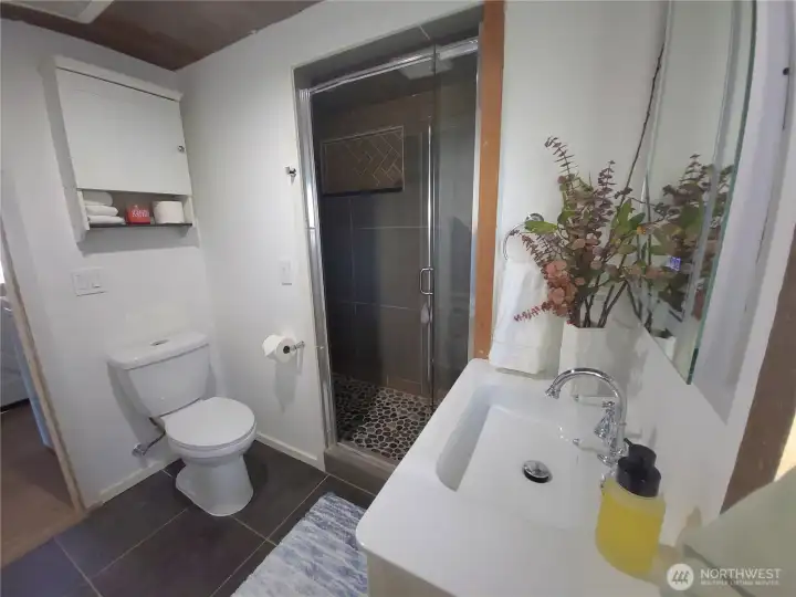 large walk-in shower with tiles and mosaic pebble floor, new glass shower door.