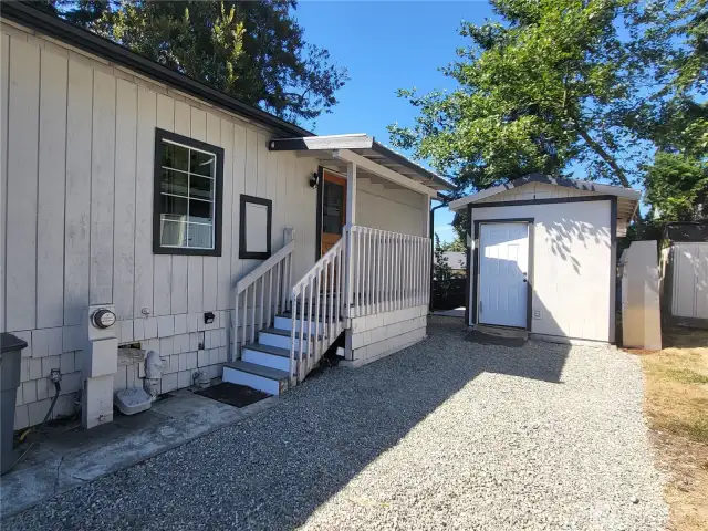 Side parking area with gravel and cement area, shed in back.
