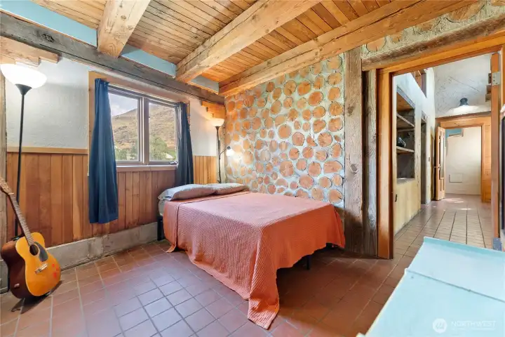 2nd bedroom down the hall from the primary.  This wing of the house features post and beam construction with stacked log filler, insulation and stucco.  This stacked wood wall was left exposed, not covered in interior plaster, to add interest and natural beauty.