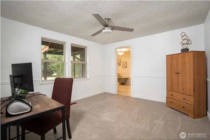 Versatile bedroom or office space filled with natural light, featuring large windows and a functional layout ideal for remote work or comfortable living. Soft carpeting, neutral tones, and easy access to the adjacent bathroom make this a flexible space to fit your needs.