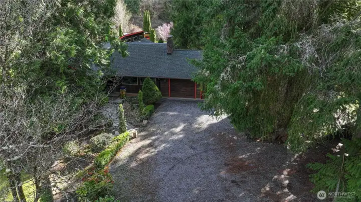 Private and inviting approach to the home, featuring a spacious driveway surrounded by mature trees and lush landscaping. The setting offers a peaceful, secluded feel with plenty of parking and a welcoming entrance that blends naturally into the serene Northwest environment.