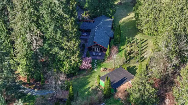 Aerial view showcasing the full beauty and privacy of the property, surrounded by mature evergreens and open usable land. The home is perfectly positioned to take advantage of the serene setting, with expansive yard space, landscaped grounds, and additional outbuildings offering versatility for hobbies, storage, or workspace. A true Pacific Northwest retreat with room to live, grow, and enjoy.