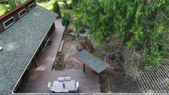 Private outdoor living space featuring an expansive deck perfect for dining and entertaining, seamlessly connected to a charming brick patio and beautifully landscaped surroundings. Nestled among mature trees, this peaceful setting offers multiple areas to relax, gather, and enjoy the natural beauty of the Pacific Northwest.