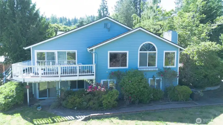 The front of the home, framed by tall evergreens and the kind of established landscaping that only comes with time. The wraparound deck goes around to a large deck and patio in the back yard.