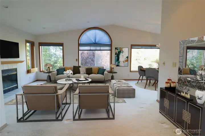 Another angle of the main living space, virtually staged, with the arched window framing a peek of the water and mountain beyond the trees.