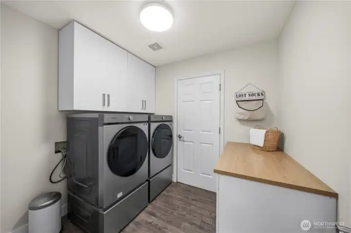 Dedicated laundry/mud room with matching front load Washer & Dryer, folding station, appliance pedestals, and ample storage.