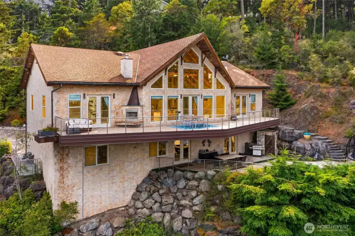 Twilight-inspired exterior view highlights the custom prow-front architecture, expansive walls of glass, broad entertaining deck, and warm interior lighting against the wooded San Juan Island setting.