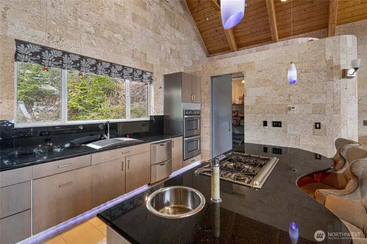 Oversized kitchen island includes a gas cooktop, prep sink, storage, and seating, with a walk-in pantry located nearby.