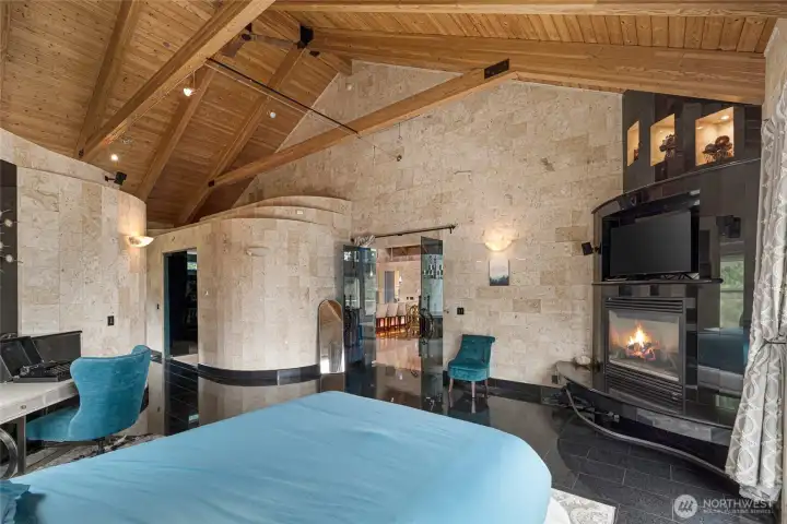 Custom stone walls, timber ceilings, integrated lighting, and a fireplace create a distinctive primary bedroom retreat.