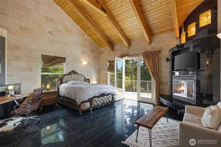Generously scaled bedroom with polished stone flooring, custom fireplace surround, timber ceilings, and access to outdoor living space.