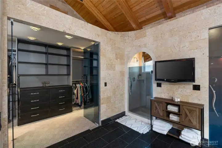 A second custom walk-in closet provides built-in drawers and hanging storage beside a glass-enclosed walk-in shower.