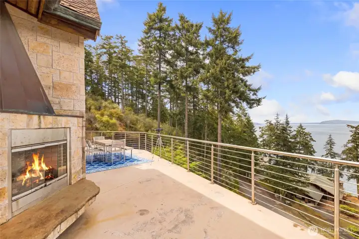 Expansive deck features an outdoor fireplace, dining area, modern railing, and scenic views across San Juan Channel.