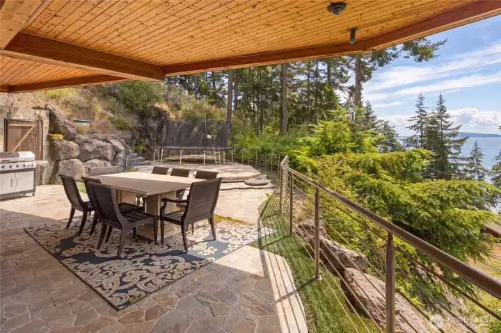 Covered stone patio offers a sheltered outdoor dining and gathering space with water views and access to the surrounding grounds.