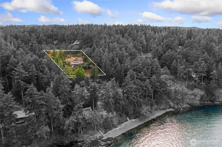 Aerial view shows the home privately positioned among mature evergreens near the shoreline of San Juan Island.