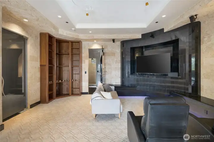 Flexible lower-level media room or guest suite features custom stonework, built-in shelving, integrated sound, and a large entertainment wall.