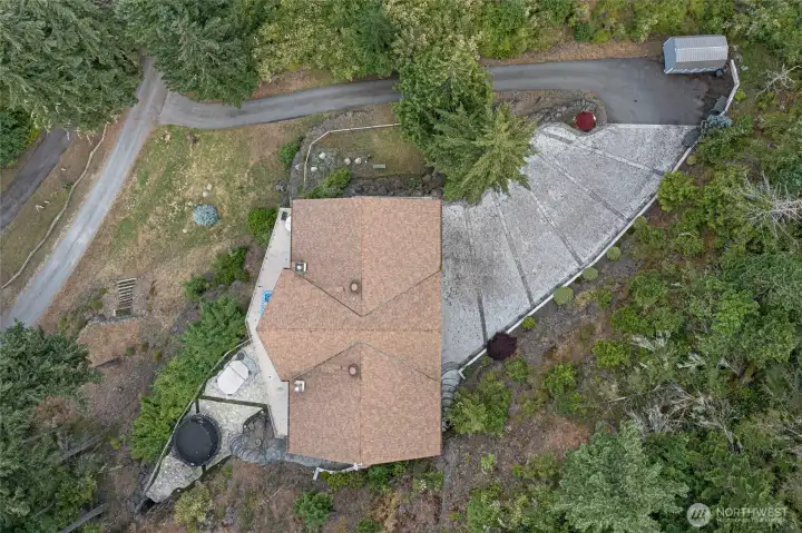 Top-down aerial view shows the residence, expansive driveway, outdoor living areas, landscaping, and surrounding mature forest.