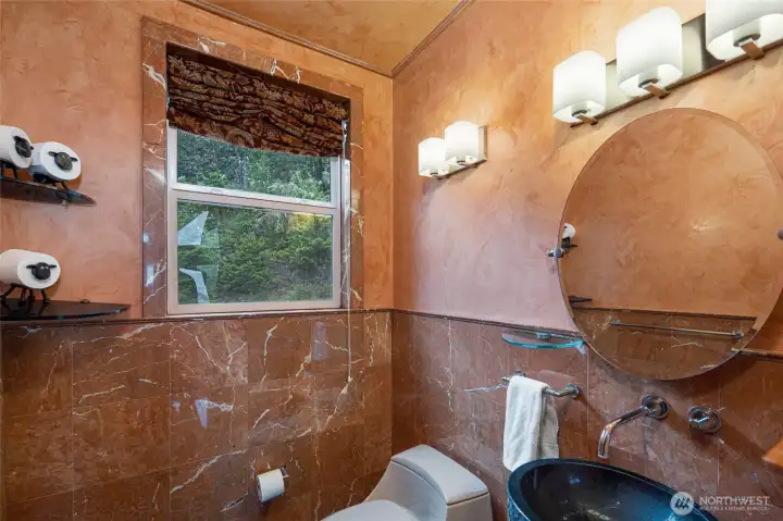 Distinctive powder room features rich stone finishes, a vessel sink, round mirror, and custom lighting.