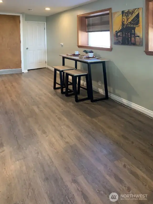 This area of the lower level is being used as the dining area. The space is large enough to hold a more traditional table. The white door in the back of the photo is a spacious pantry. The wood door on the left side of this photo is the interior access to the main floor.