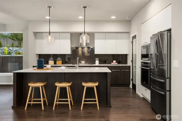 Generous slab quartzite island with upgrade pendant lighting. Walk in pantry door is to the right.