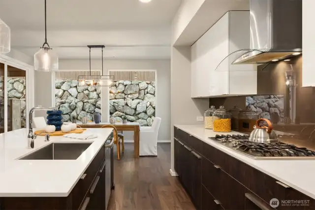 So much storage in the clean lined cabinetry. Gas range is on display with the rich slab backsplash and glass top hood.