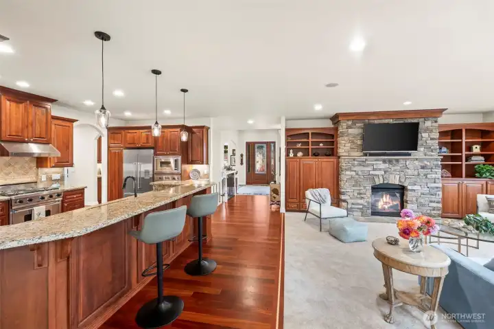Expansive great room blending living, kitchen, and dining, anchored by rich hardwoods, custom cabinetry, and a floor-to-ceiling stone fireplace.