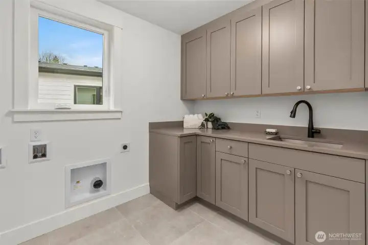 Well appointed laundry room with custom cabinets, slab counters, and stainless steel sink